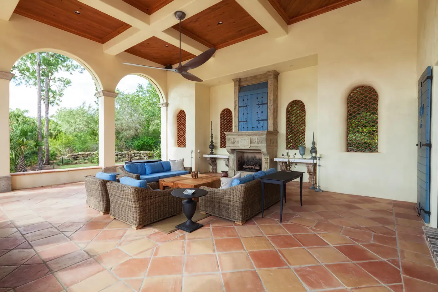 Loggia cubierta de estilo mediterráneo con ventilador de techo moderno, techo de madera artesonado y chimenea de piedra