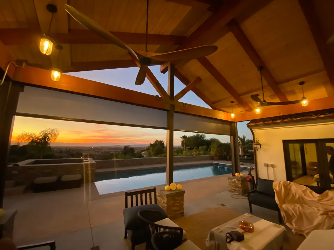 Patio cubierto al atardecer con dos ventiladores de techo de madera y alberca con vista a las colinas
